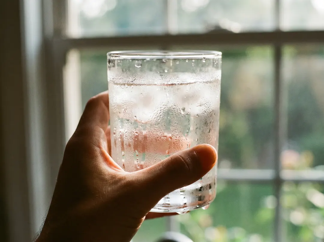 Hand holding a glass of water against a sunlit window